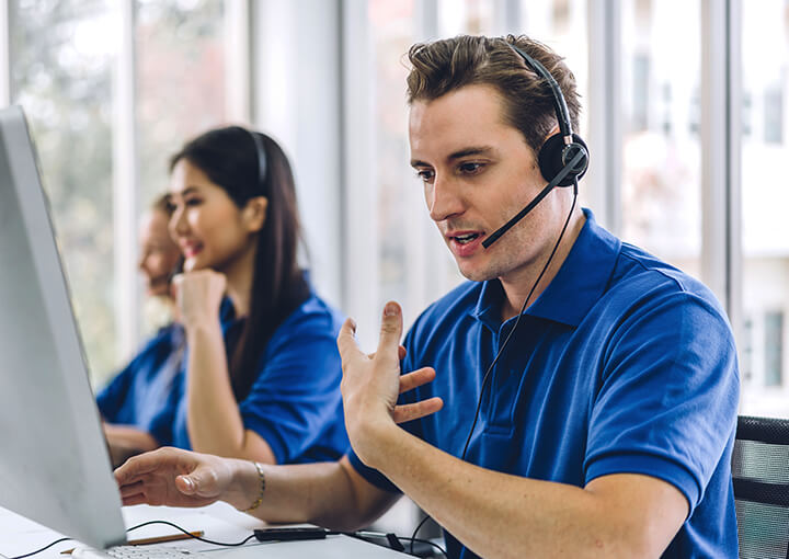 man in focus in a call center office with headphones speaking to a client